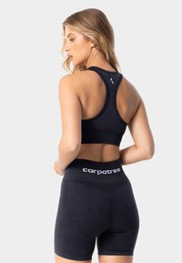 Melnas sporta krūšturis ar šķērsgriezuma dizainu, ko pavada melnas augstās vidukļa bikses ar baltu "carpatree" logotipu uz jostas.