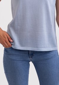 Světle modrý tílko bez rukávů vyrobené z měkké tkaniny, které je kombinováno s úzkými džíny. Tílko má jemnou strukturu a rovný lem.