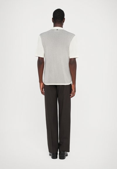 Gray ribbed knit short-sleeve top with white accents, paired with black loose-fitting trousers and black footwear. Flat back view.