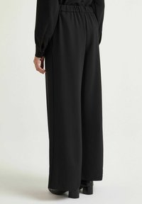 Pantaloni neri a gamba larga con vita elasticizzata, caratterizzati da una texture di tessuto liscia e gambe di lunghezza normale e taglio dritto.