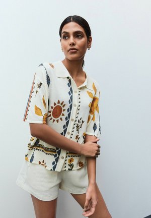 Knit cardigan in cream with floral and geometric patterns in yellow, orange, and blue; short sleeves; button front; classic collar.