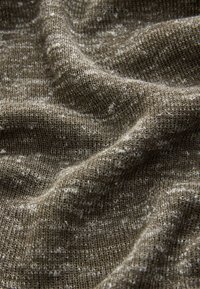 Primo piano di tessuto marrone lavorato a maglia con un motivo strutturato e fibre visibili, che mostra pieghe morbide e ombre.