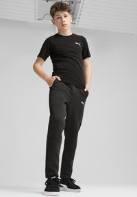 Melna īsā piedurkņu T-kreklā un melnos sporta biksēs no Puma, ar baltu logo. Apģērbu raksturo vienkāršs dizains un pieguļošs siluets.