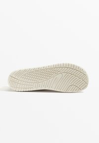 White rubber sole with textured tread pattern. Features grooves and contours for traction. No visible logos or distinctive markings.