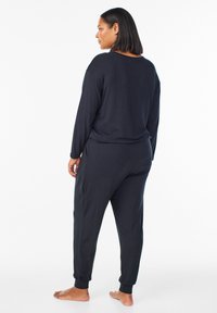 Zwarte loungewear set met een langwerpige top en tapse pantalons met ribbelmanchetten. Zacht materiaal met een relaxte pasvorm, ontworpen voor comfort.