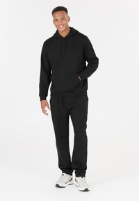 Felpa nera con tasca a marsupio, pantaloni jogger neri coordinati e scarpe da ginnastica di colore chiaro. Design semplice e tessuto morbido.