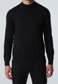Black sweater with a high neckline, long sleeves, and ribbed cuffs. Made from a soft fabric. Features a small, subtle logo on the chest.