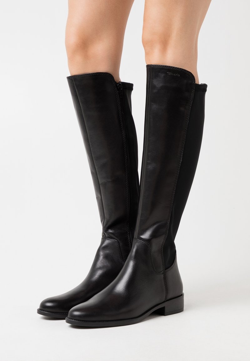 Bottes en cuir noir arrivant au genou avec une finition lisse, fermeture éclair latérale verticale et un petit talon carré. Présente un design ajusté pour une silhouette élégante.