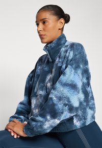 Fleece pullover jacket with a high collar, zip closure, and a blue tie-dye pattern. Features loose sleeves and a front pocket.