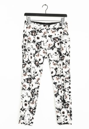 Pantaloni bianchi aderenti con motivo floreale nero e rosa chiaro appesi a una gruccia nera su uno sfondo bianco.
