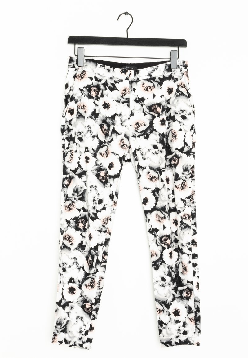 Pantalon blanc slim avec motif floral noir et rose clair suspendu à un cintre noir sur un fond blanc.