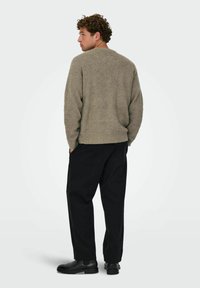 Suéter verde de gran tamaño y textura con cuello redondo, combinado con pantalones negros ajustados y botines negros, visto desde la espalda.