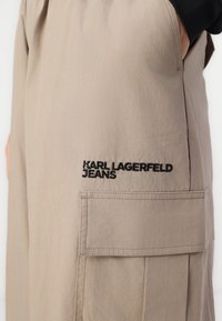 Béžové cargo nohavice so vyšívaným logom "KARL LAGERFELD JEANS". Obsahujú bočnú kapsu a majú hladký, jemný povrch.