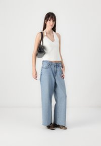 White halter top with a v-neckline, wide light blue jeans, black handbag, and leopard print flats. Smooth fabric and relaxed fit.