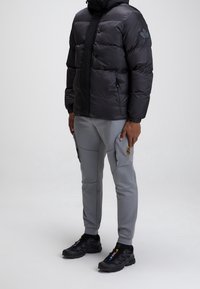 Doudoune noire avec fermeture éclair et bouton, associée à un pantalon slim gris avec poches cargo et des baskets noires.