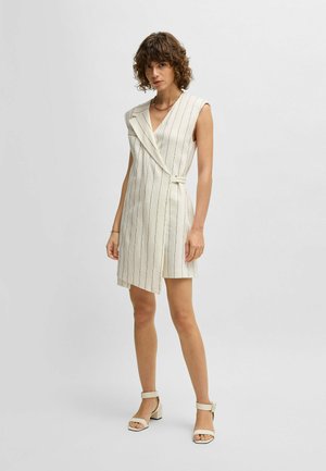 Ärmelloses cremefarbenes Kleid mit vertikalen schwarzen Streifen, Wickeldesign und einem Bindegürtel. Glatte Textur und knielang, kombiniert mit beigen Blockabsatzsandalen.