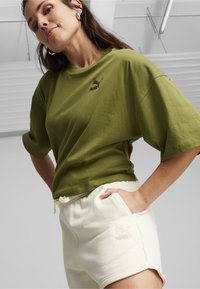 Maslinasto zeleni pamučni T-shirt s crnim Puma logom, uparen s krem šortsevima s bočnom džepom i izvezenim logom.