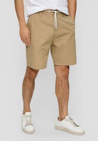 Beige Shorts aus leichtem Material mit einem Kordelzugbund und seitlichen Taschen, getragen mit weißen Sneakers.