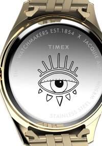 Rückseite der Uhr in Goldton mit einem eingravierten Augendesign, Timex-Logo und Text über Zusammenarbeit und Edelstahlmaterial.