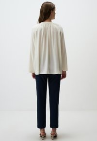 Blusa crema con dettaglio arricciato sul retro, maniche lunghe e scollo rotondo abbinata a pantaloni blu navy e sandali con tacco beige.