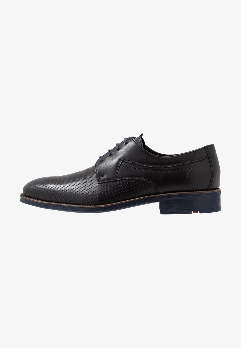 Chaussure habillée pour homme en cuir noir avec bout perforé, fermeture à lacets et détails de trépointe marron sur une semelle noire à petit talon.
