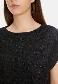 Schwarzes Oberteil mit aufwendiger floralem Stickerei und Perlen entlang des Ausschnitts. Weicher Stoff mit strukturierter Oberfläche. Rundhalsausschnitt-Design.
