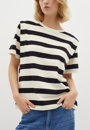 Svart och vit randig t-shirt med rund hals, korta ärmar, mjukt bomullsmaterial och en avslappnad passform. Bomullsdenim shorts under.