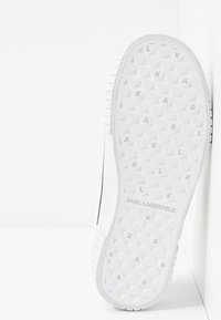 Weißer Sneaker mit einer strukturierten Gummisohle, die ein geometrisches Muster aufweist, mit der Markierung "KARL" und schwarzen Akzenten an den Seiten.