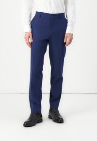 Pantalons ajustés navy en tissu lisse, avec une taille plate, une coupe droite et des poches latérales, associés à des bottes en cuir noires.
