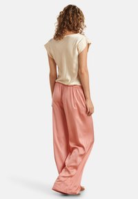 Top corto a maniche corte color crema abbinato a pantaloni larghi in satin rosa con vita elastica, che mettono in risalto trame morbide e un design fluido.