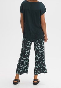 Tmavě zelený top s krátkými rukávy, doplněný širokými kalhotami s černým a mátově zeleným vzorem s abstraktním květinovým motivem.