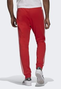 Pantaloni sportivi rossi con strisce laterali bianche, vestibilità affusolata e polsini a costine. Indossati con sneakers in bianco e nero con un logo classico.