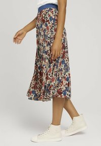 Jupe midi florale avec des couleurs rouge, bleu et crème. Taille élastique bleue, design plissé, associée à des baskets montantes crème.