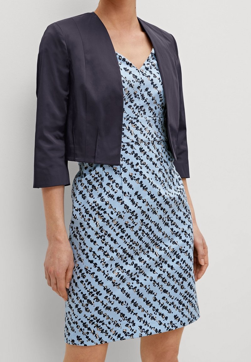 Marinblå kort jacka över en ljusblå klänning med en spridd svart och vit abstrakt mönster, med V-hals och figurnära passform.