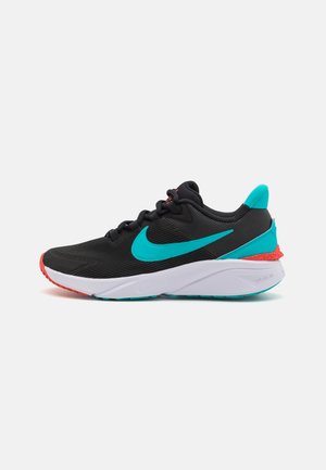 Svart athletic sko med tealfarget aksenter og rød såle. Har teksturert overdel, polstret hvit mellomsåle og fremtredende Nike swoosh-logo.