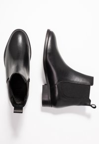 Botines de cuero negro con un acabado suave, paneles laterales elásticos y una pequeña lengüeta en la parte posterior; tacón bajo y punta redonda.