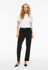 Juodos siaurėjančios kelnės su elastine juosmens juosta ir raišteliais, derinamos su balta trumpomis rankovėmis marškinėliais. Modelis dėvi juodus aukštakulnius.