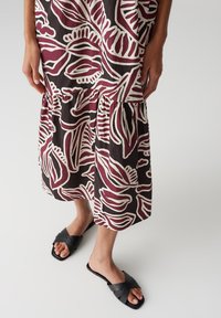 Abito midi floreale in marrone scuro e crema, con orlo a strati e un audace motivo a foglie. Abbinato a sandali neri a tracolla.