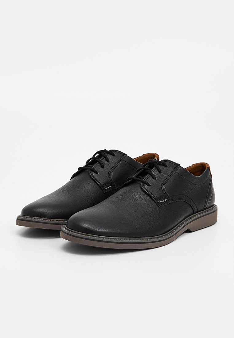 Scarpe di pelle nera con punta rotonda, design classico con lacci e dettagli di cucitura sulla parte superiore. Suola in gomma con leggera texture e contrasto.