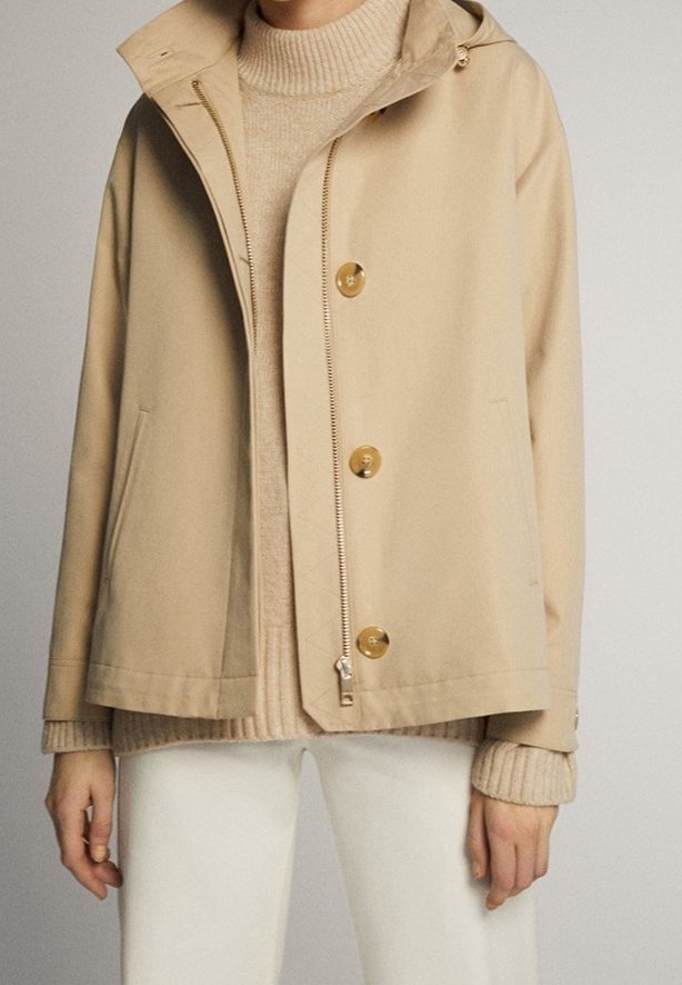 Beige jas met een capuchon, rits en grote knopen, met twee zijzakken en een ontspannen pasvorm, gelaagd over een lichte trui.