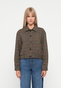 Veste cropped en vichy marron avec des accents rouges, dotée d'un col et de cinq boutons noirs sur le devant. Portée sur un denim taille haute.