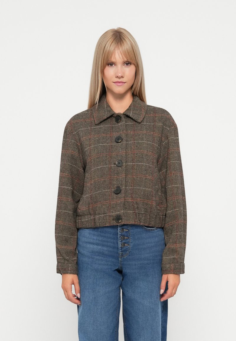 Veste cropped en vichy marron avec des accents rouges, dotée d'un col et de cinq boutons noirs sur le devant. Portée sur un denim taille haute.