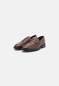 Mocassins habillés marron en cuir à enfiler, semelle noire, bout arrondi, avec le nom de la marque embossé sur le devant, présentés sur fond blanc.