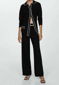 Ensemble noir en deux pièces comprenant une chemise à manches longues avec des accents crème et un pantalon large en tissu doux et texturé.