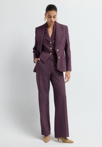 Costume sur mesure violet avec une veste à double boutonnage, des revers crantés et des boutons dorés. Comprend un pantalon à jambes larges et une texture lisse.