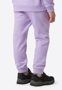 Lila Jogginghose mit weicher Textur, schmaler Passform und elastischen Bündchen; kombiniert mit schwarzen Sportschuhen mit grauen Akzenten und einer robusten Sohle.