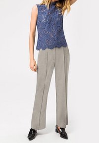 Top sin mangas de encaje azul con estampado floral y dobladillo en forma de pico, combinado con pantalones de pierna ancha de color gris claro y zapatos de charol negros.