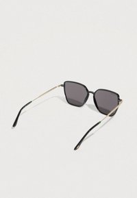 Čierne štvorcové slnečné okuliare s tmavými sklami. Kovové zlaté detaily na ramenách s textúrovaným vzorom a zeleným zakončením.