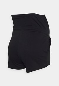 Pantaloni sportivi neri con vita alta e una texture liscia. Presentano una tasca laterale e un design semplice per comfort e libertà di movimento.