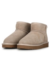 Botas de tobillo de ante beige con punta redondeada, costuras mínimas, textura suave y suela plana de goma con un patrón antideslizante.